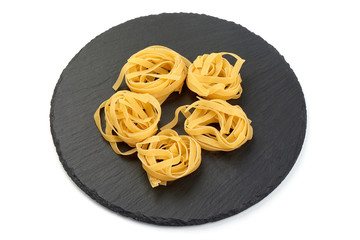 Raw tagliatelle pasta on a slate shale plate, Itallian food, close-up, isolated on white background