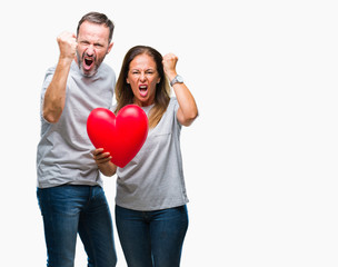 Fototapeta na wymiar Middle age hispanic casual couple in love holding red heart over isolated background annoyed and frustrated shouting with anger, crazy and yelling with raised hand, anger concept