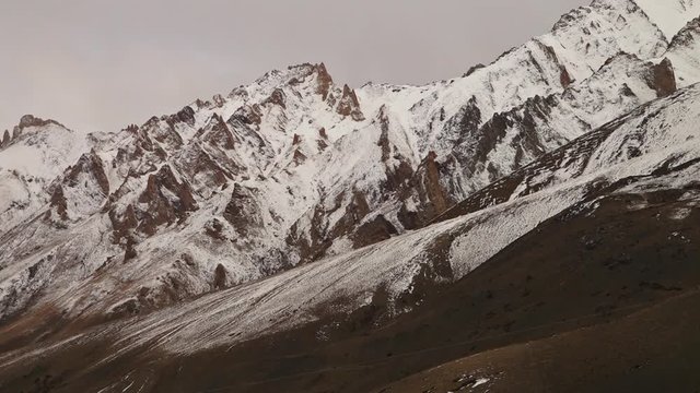 Close up, low angle still shot of steep slopes of Indian Himalayan ranges with sharp parallel ar tes partially covered by snow ice.