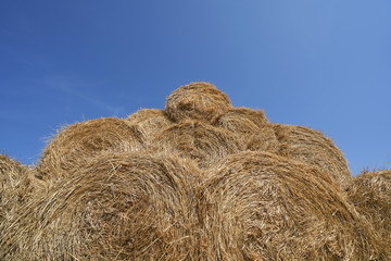 Big haystack from round bales laid in the form of a pyramid against the blue sky
