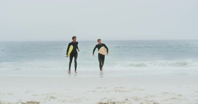 Front view of two male surfers running together with surfboard on the beach 4k
