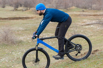 A guy in sportswear riding clothes on a modern mountain carbon bike with an air suspension fork at a vintage brick concrete wall.	