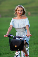 Fototapeta premium Soft focus photo. A young, beautiful blond woman with a white bike in a green meadow.