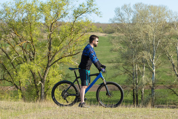 Obraz premium Cyclist in shorts and jersey on a modern carbon hardtail bike with an air suspension fork rides off-road on green hills near the forest 