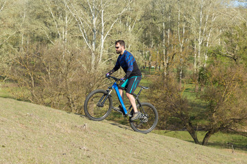 Fototapeta premium Cyclist in shorts and jersey on a modern carbon hardtail bike with an air suspension fork rides off-road on green hills near the forest 