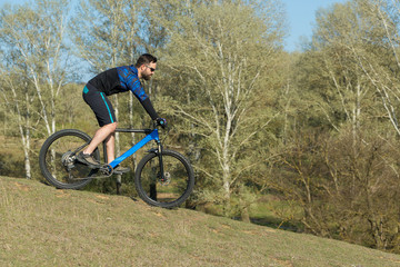 Fototapeta premium Cyclist in shorts and jersey on a modern carbon hardtail bike with an air suspension fork rides off-road on green hills near the forest 