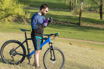 Fototapeta premium Cyclist in shorts and jersey on a modern carbon hardtail bike with an air suspension fork rides off-road on green hills near the forest 
