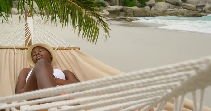 Front view of African american woman sleeping in a hammock on the beach 4k