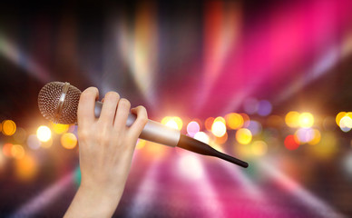 A female hand is holding one microphone against the colorful lights of the karaoke club scene. Bright colorful background with blurred neon lights