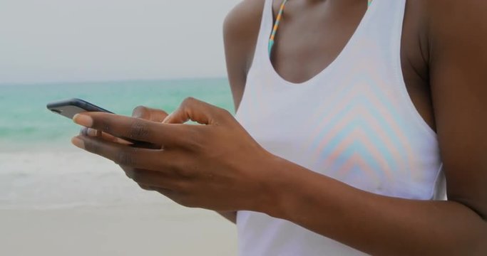 Front view of African American woman using mobile phone on the beach 4k