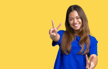 Young beautiful brunette woman wearing blue t-shirt over isolated background smiling looking to the camera showing fingers doing victory sign. Number two.