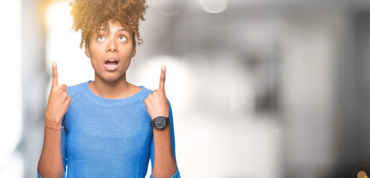 Beautiful young african american woman over isolated background amazed and surprised looking up and pointing with fingers and raised arms.