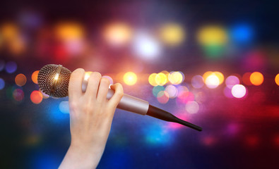 A female hand is holding one microphone against the colorful lights of the karaoke club scene....