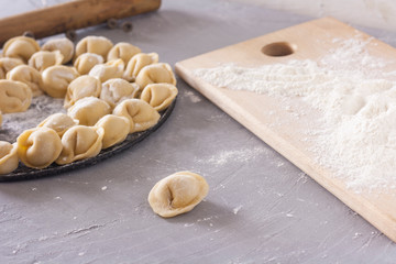 Homemade ravioli on a round platter on the table with flour and rolling pin
