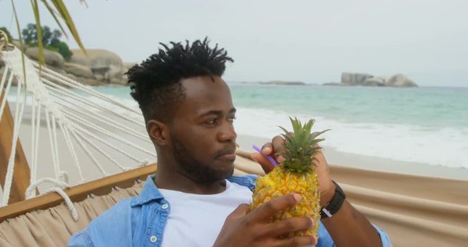 Front view of African american man drinking pineapple juice on the beach 4k