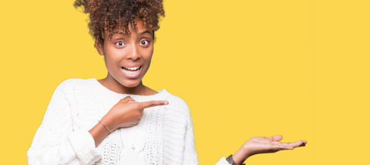 Beautiful young african american woman wearing winter sweater over isolated background amazed and smiling to the camera while presenting with hand and pointing with finger.