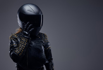 Portrait of a biker girl wearing leather racer costume and protective helmet in a studio on a gray...