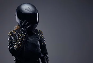 Foto op Plexiglas Portrait of a biker girl wearing leather racer costume and protective helmet in a studio on a gray background. © Fxquadro