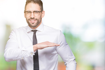 Young handsome business man wearing glasses over isolated background gesturing with hands showing big and large size sign, measure symbol. Smiling looking at the camera. Measuring concept.