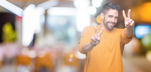 Young handsome man over isolated background smiling looking to the camera showing fingers doing victory sign. Number two.