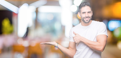 Handsome man wearing white t-shirt over night outdoors background Showing palm hand and doing ok gesture with thumbs up, smiling happy and cheerful