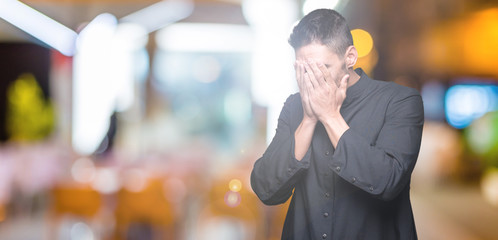 Young Christian priest over isolated background with sad expression covering face with hands while...