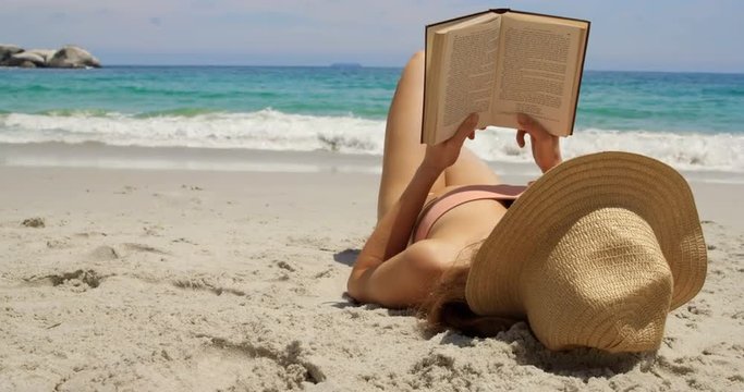 Caucasian woman in hat reading a book on the beach 4k