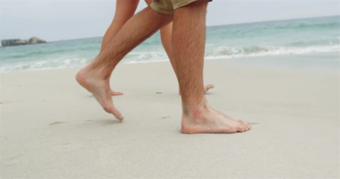 Low section of couple walking barefoot on the beach 4k