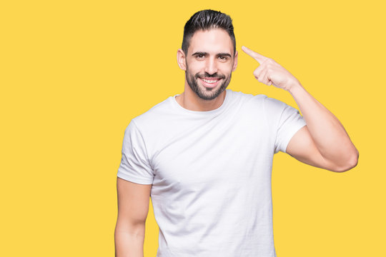 Handsome man wearing white t-shirt over yellow isolated background Smiling pointing to head with one finger, great idea or thought, good memory