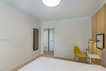 Simple bedroom interior with bed, small glass table , white bedding and wardrobe