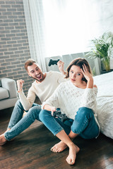 Obraz premium happy man looking at upset girl sitting on floor with joystick
