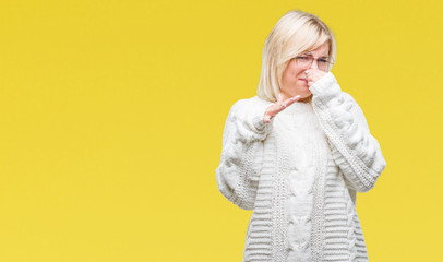 Young beautiful blonde woman wearing winter sweater and glasses over isolated background smelling...