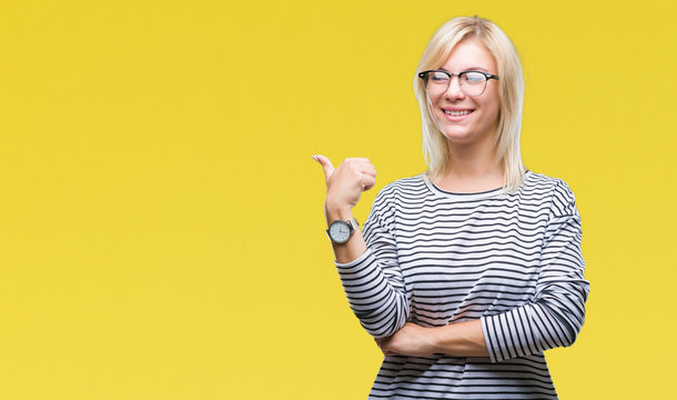 Young beautiful blonde woman wearing glasses over isolated background smiling with happy face looking and pointing to the side with thumb up.