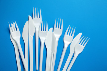 White plastic knives and forks. Disposable plastic tableware on blue background, top view