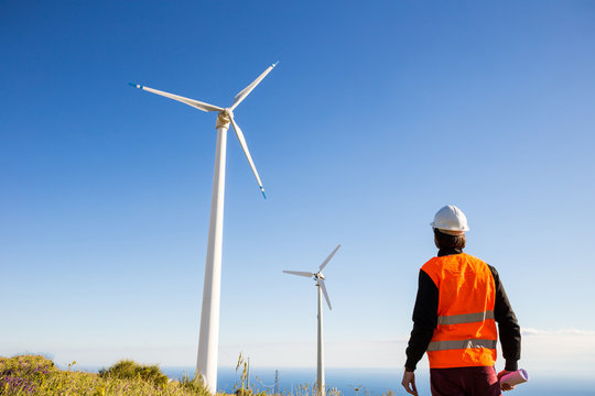 Ingegnere elettrico controlla l'impianto eolico con il gilet ad alta visibilit&agrave; e casco bianco. Progetto in mano. Concetto di manutenzione