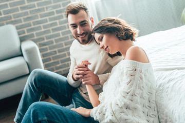 happy man holding hands with attractive girlfriend while sitting on floor at home