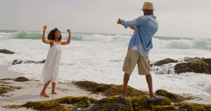 Rear view of African american man clicking photos of woman with mobile phone on the beach 4k