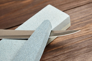 Whetstones and steel knife blade. Grindstones. Oval and rectangular double layer sharpening stone on wooden table background