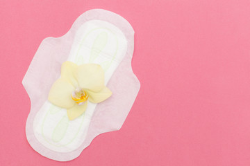 Top view of women's sanitary pad and orchid on a pink background with space for text. flat lay