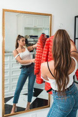 Young woman in a blu jeance white t-shirt trying on red down coat in a luxury boutique
