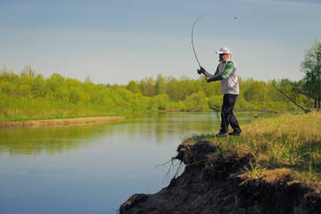 Man fish with spinning on river bank, casting lure. Outdoor weekend activity. Photo with shallow...