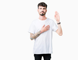 Young handsome man wearing white t-shirt over isolated background Swearing with hand on chest and...