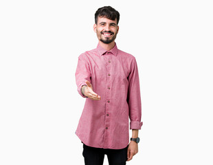 Fototapeta premium Young handsome man wearing pink shirt over isolated background smiling friendly offering handshake as greeting and welcoming. Successful business.