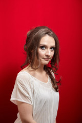 Portrait of young woman on red background. Attractive lady with long wavy brown hair in white blouse