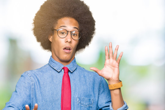 Young african american business man with afro hair wearing glasses and red tie afraid and terrified with fear expression stop gesture with hands, shouting in shock. Panic concept.