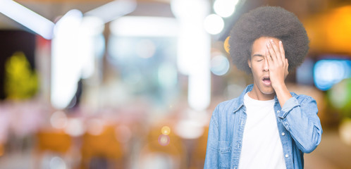 Young african american man with afro hair Yawning tired covering half face, eye and mouth with...
