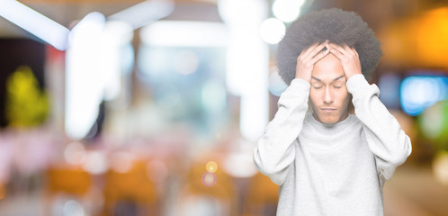 Young african american man with afro hair wearing sporty sweatshirt suffering from headache desperate and stressed because pain and migraine. Hands on head.