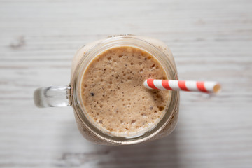 Glass jar filled with banana, kiwi, apple smoothie on a white wooden background, top view. Flat lay, from above, overhead.