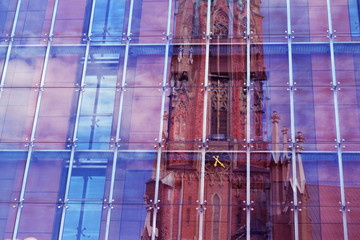 Reflection of a 19th-century neo-gothic cathedral in a glass facade of a modern building