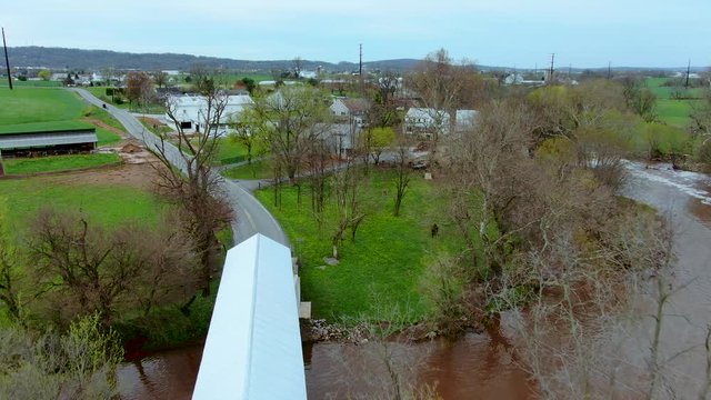 Covered bridge spans a river in rural landscape, Bitzer's Mill bridge on Conestoga river in Lancaster county, Pennsylvania, aerial flyover